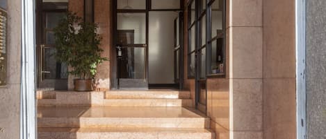 A building entrance with marble steps, a potted plant, and a glass door.