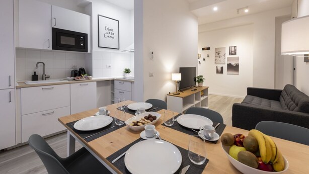 Een moderne keuken met witte kasten, een magnetron en een eethoek met een houten tafel voor vier personen.