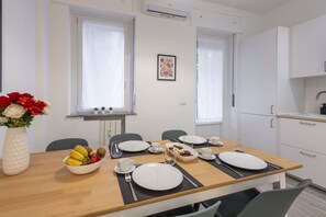 Ein zeitgemäßer Essbereich mit einem Holztisch, gedeckt für vier Personen, weißen Tellern, Besteck und einer Obstschale.