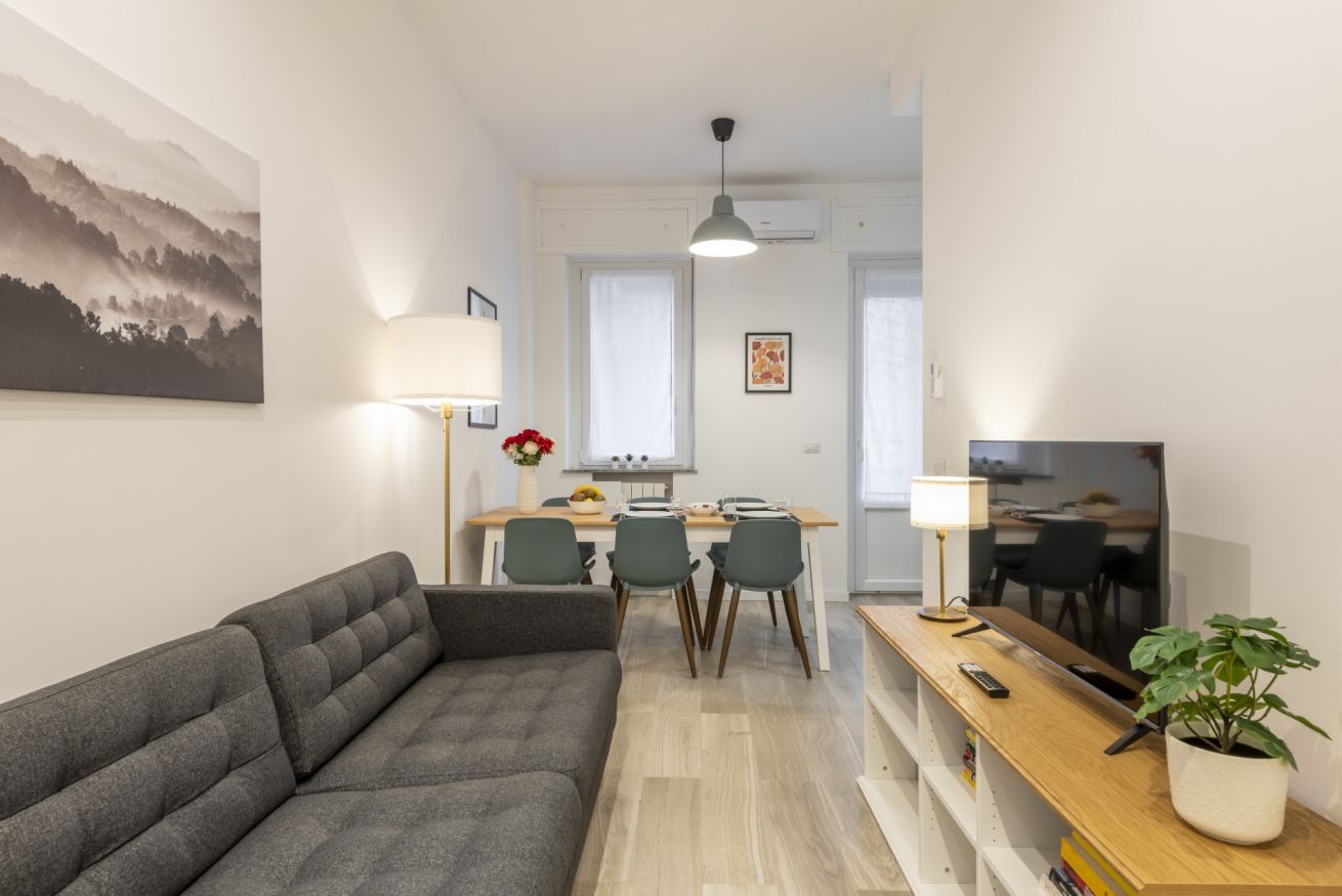 A modern living room with a sofa, dining area with chairs, a TV, and a plant.
