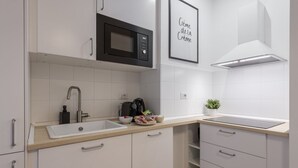 Een moderne keuken met witte kasten, een zwarte magnetron, een spoelbak en een lijst met een bord boven het fornuis.