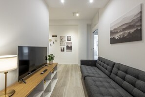 Un salon moderne avec un téléviseur à écran plat, un canapé, une console en bois, une lampe et une plante en pot.