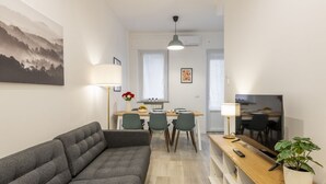 Een moderne woonkamer met een bank, een eethoek met stoelen, een televisie en een plant.