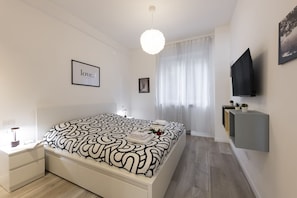 A modern bedroom with a large bed, a bedside table, a mounted TV, and a framed picture on the wall.