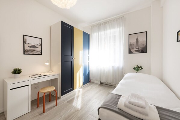 A modern hotel room with a bed, desk, chair, and a large window with curtains.