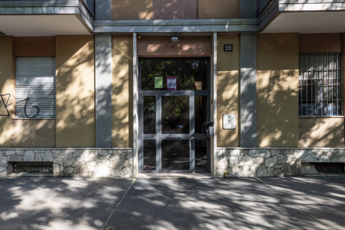 A building entrance with a glass door, a number '28' sign, and a security camera above the door.