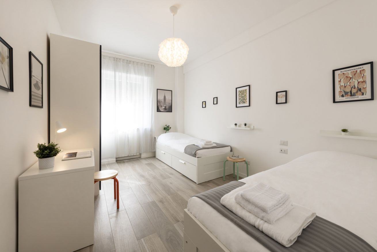 A modern hotel room with a bed, a desk, a chair, a small table, and a mirror.