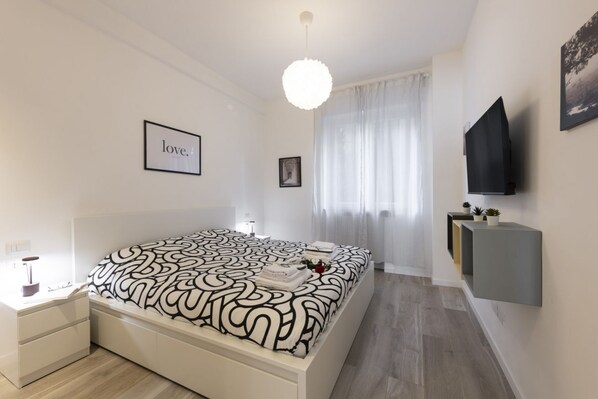 A modern bedroom with a large bed, a bedside table, a mounted TV, and a framed picture on the wall.