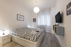 A modern bedroom with a large bed, a bedside table, a mounted TV, and a framed picture on the wall.