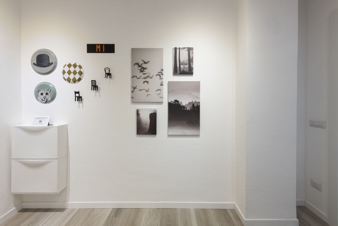 A minimalist room with a white wall, a small white cabinet, and several framed pictures.