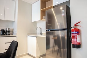 A modern kitchen with a stainless steel refrigerator, a coffee maker, and a fire extinguisher mounted on the wall. - Bloomfields Stylish 1BR in Reflection (Abu Dhabi)