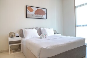 A hotel room with a large bed, a bedside table with a lamp, a wall-mounted artwork, and a window providing natural light. - Bloomfields Stylish 1BR in Reflection (Abu Dhabi)