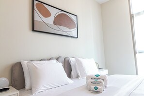 A hotel room with a bed, pillows, a nightstand, a lamp, a framed abstract artwork, and a window. - Bloomfields Stylish 1BR in Reflection (Abu Dhabi)