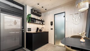 A modern kitchen with a black countertop, built-in shelves, and a black cabinet. There is a dining table with chairs and a vase with flowers. - Heathland Lodge (Selfoss)