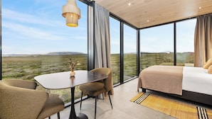 A modern room with a large window, a bed, a table, and two chairs. - Heathland Lodge (Selfoss)