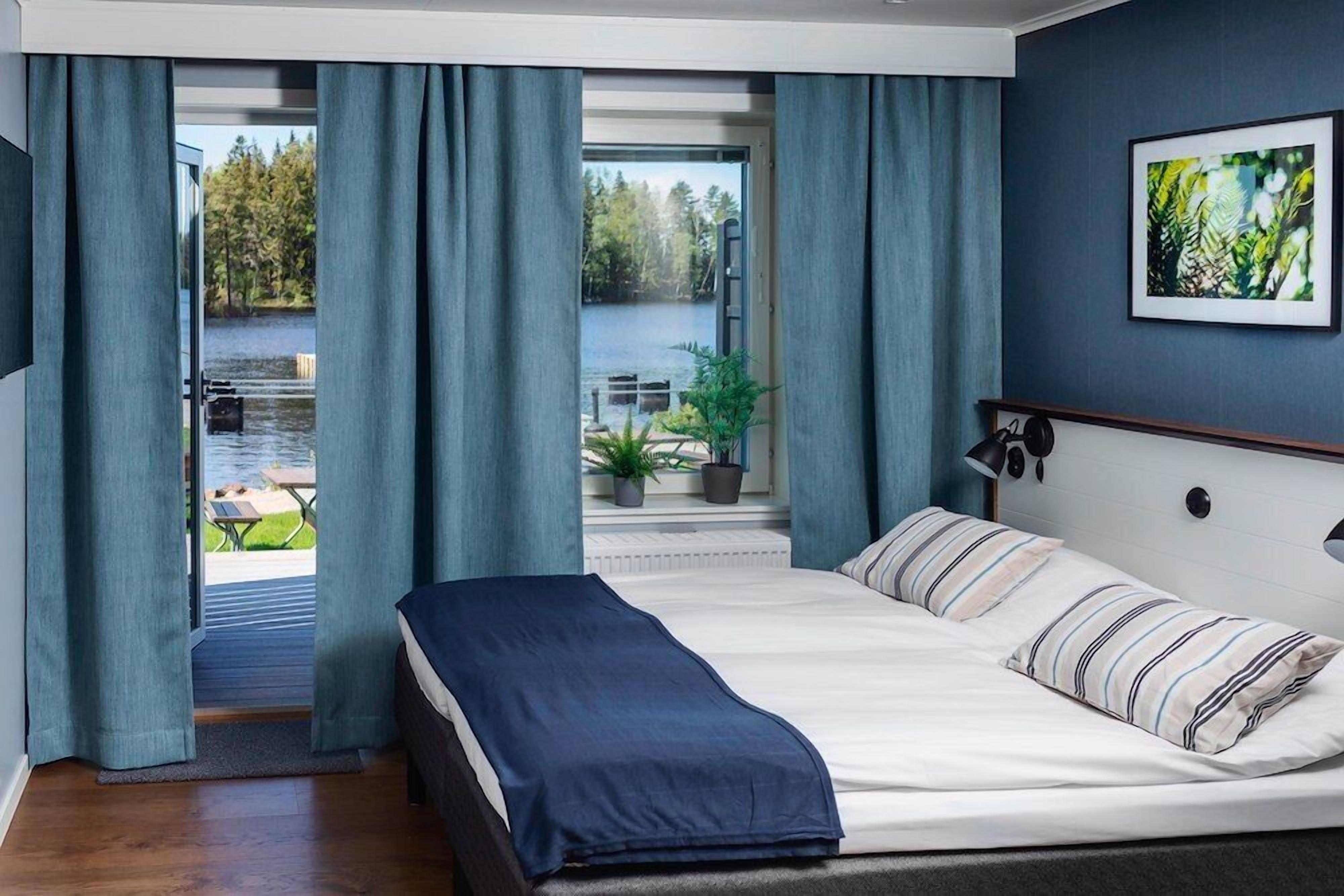 Een slaapkamer met een bed, uitzicht op een meer en een eethoek met terrasmeubels.
