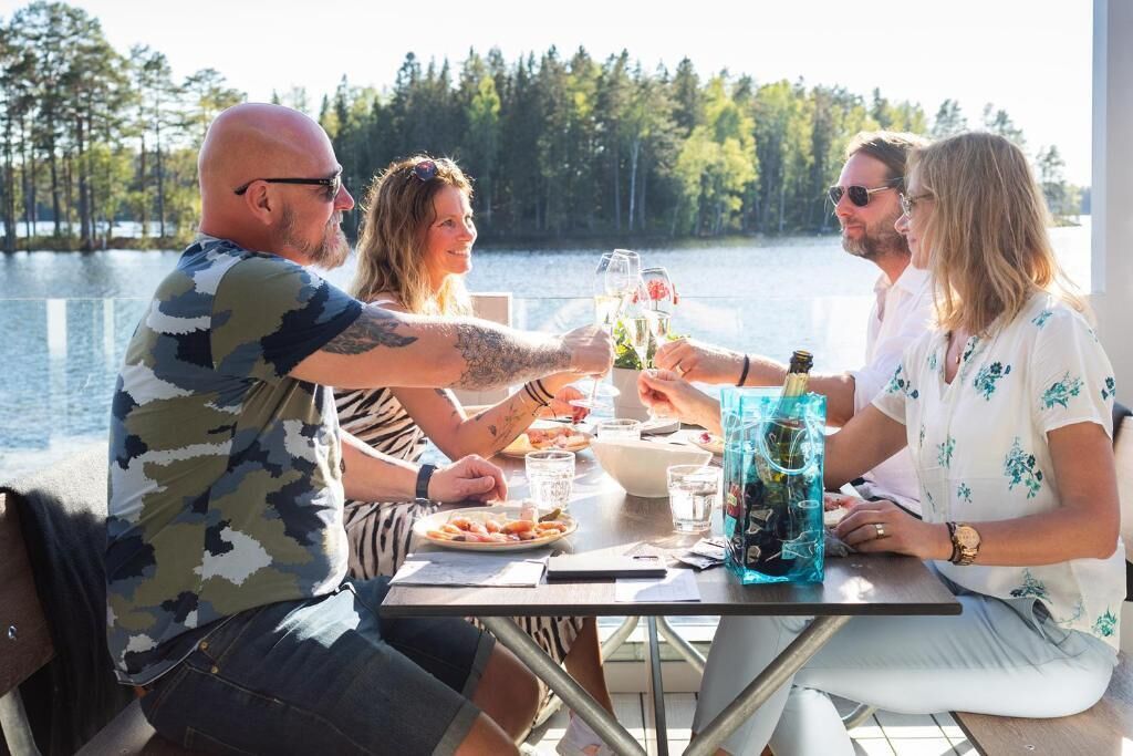 Un grupo de personas sentadas en una mesa junto a un lago, con bebidas y comida sobre la mesa.