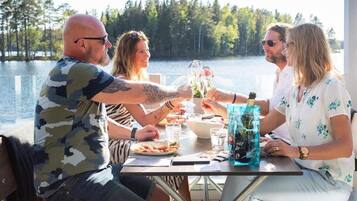 Un grupo de personas sentadas en una mesa junto a un lago, con bebidas y comida sobre la mesa.