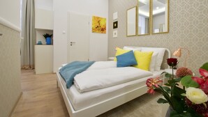 A bedroom with a bed, a bedside table, a mirror, and a vase with flowers. - St King 11. Studio Apartments (Budapest)