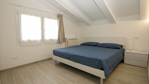 Un dormitorio con cama, mesita de noche, lámpara y ventana con cortinas.
