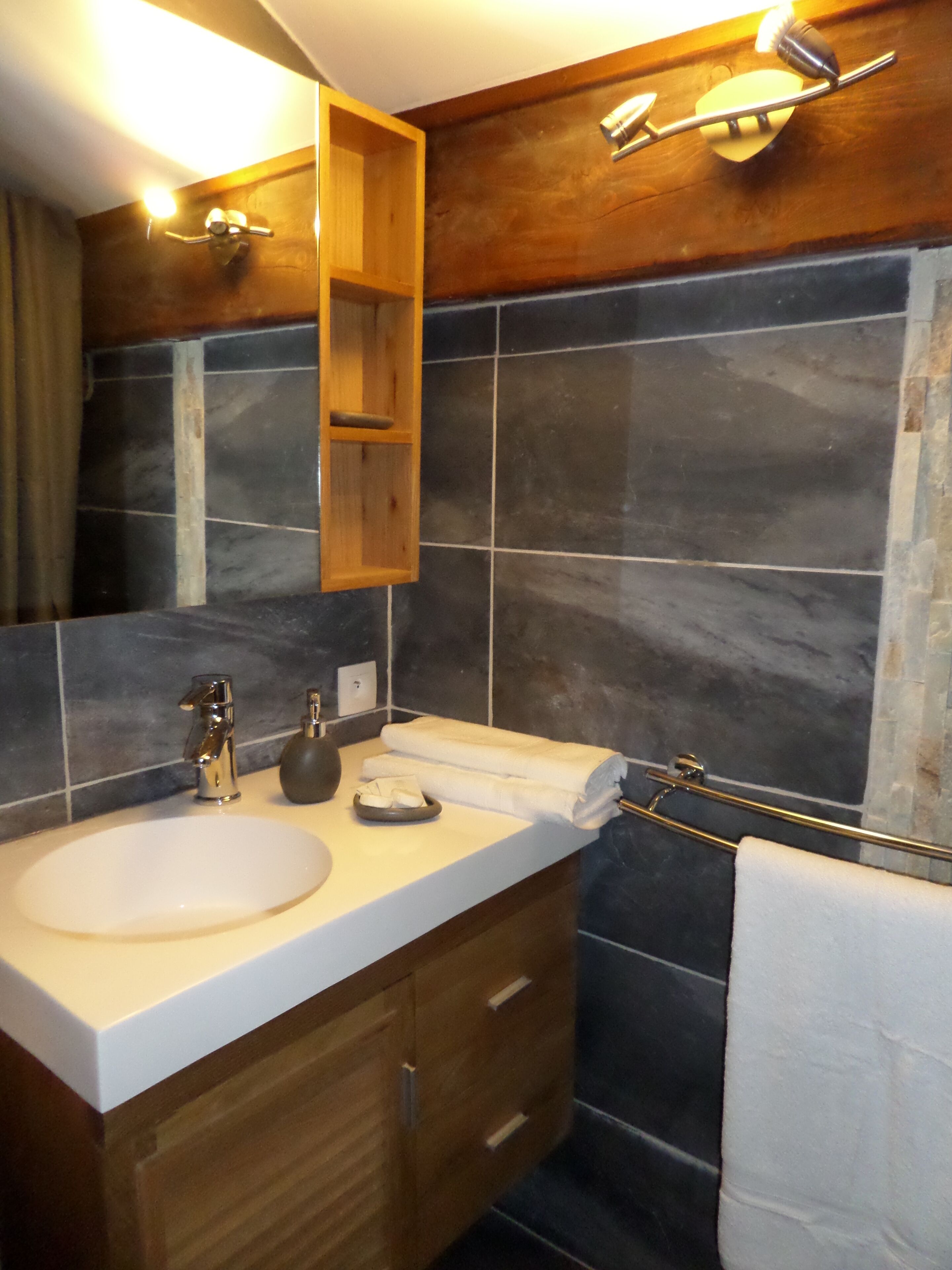 A bathroom with a wooden vanity, a white sink, a towel rack, and a mirror.