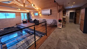 Amplio espacio interior con piso de madera, jacuzzi, asientos y televisor montado en la pared.