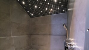Un área de ducha moderna con un banco, techo de diseño enrejado y cabezal de ducha montado en la pared.