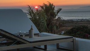 Un área de descanso iluminada por el sol con vista a la puesta de sol sobre el mar, una botella y dos vasos sobre una mesa.