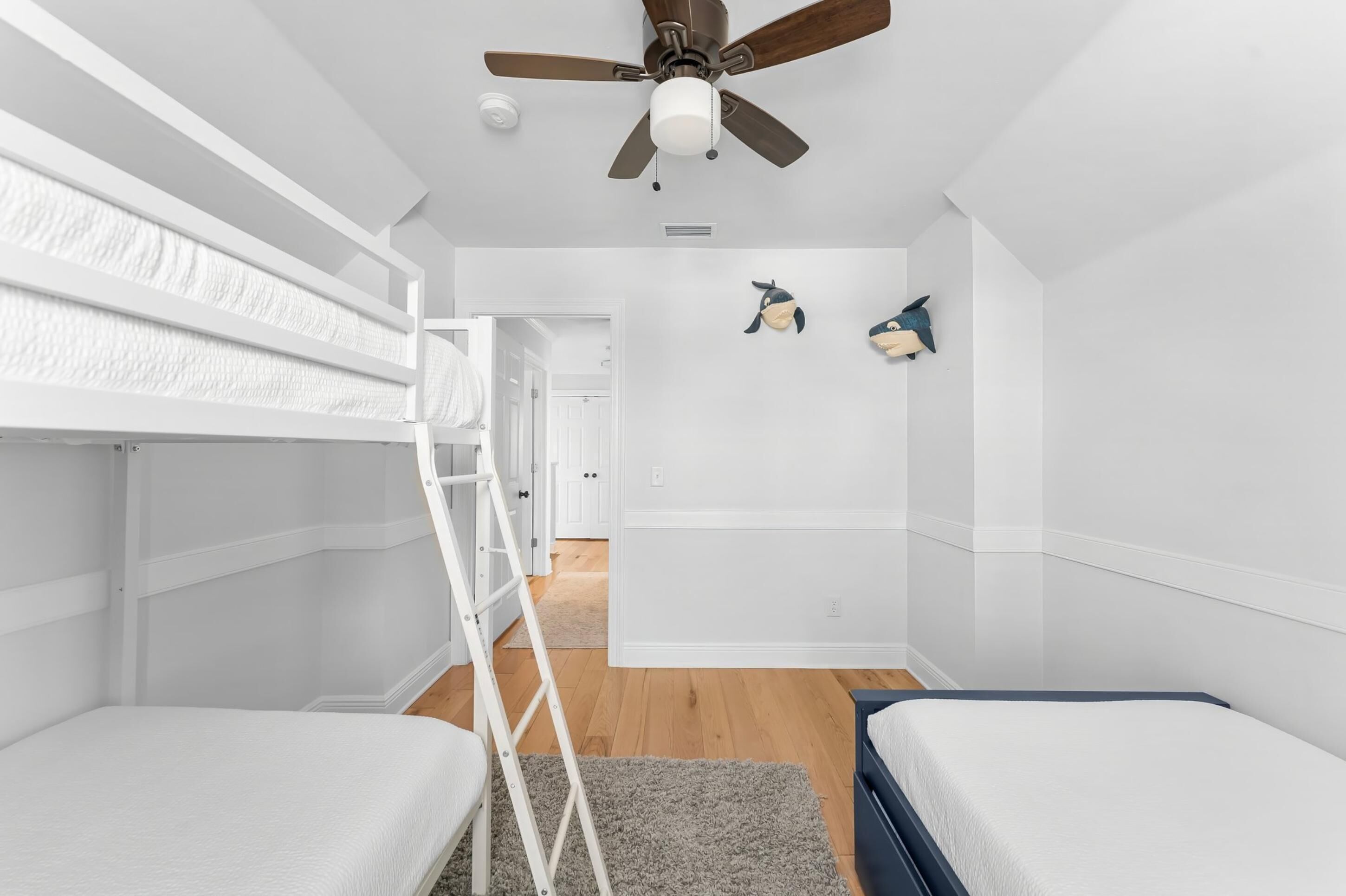 Una habitación con literas, ventilador de techo y una puerta que da a otra estancia.