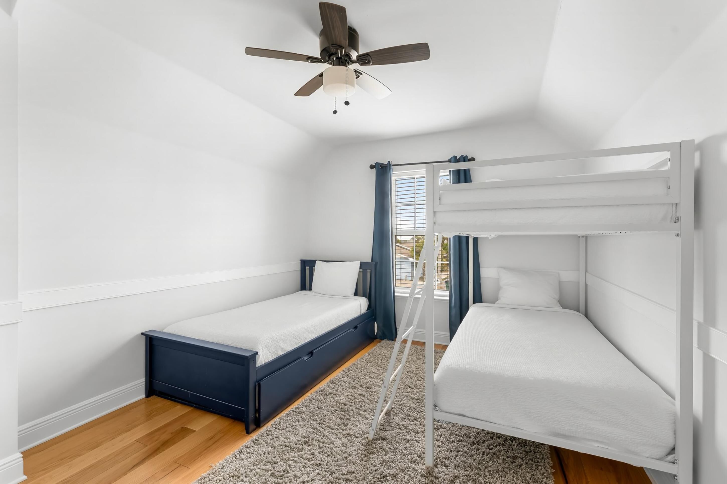 Une chambre avec deux lits, un ventilateur de plafond et une fenêtre avec des rideaux.