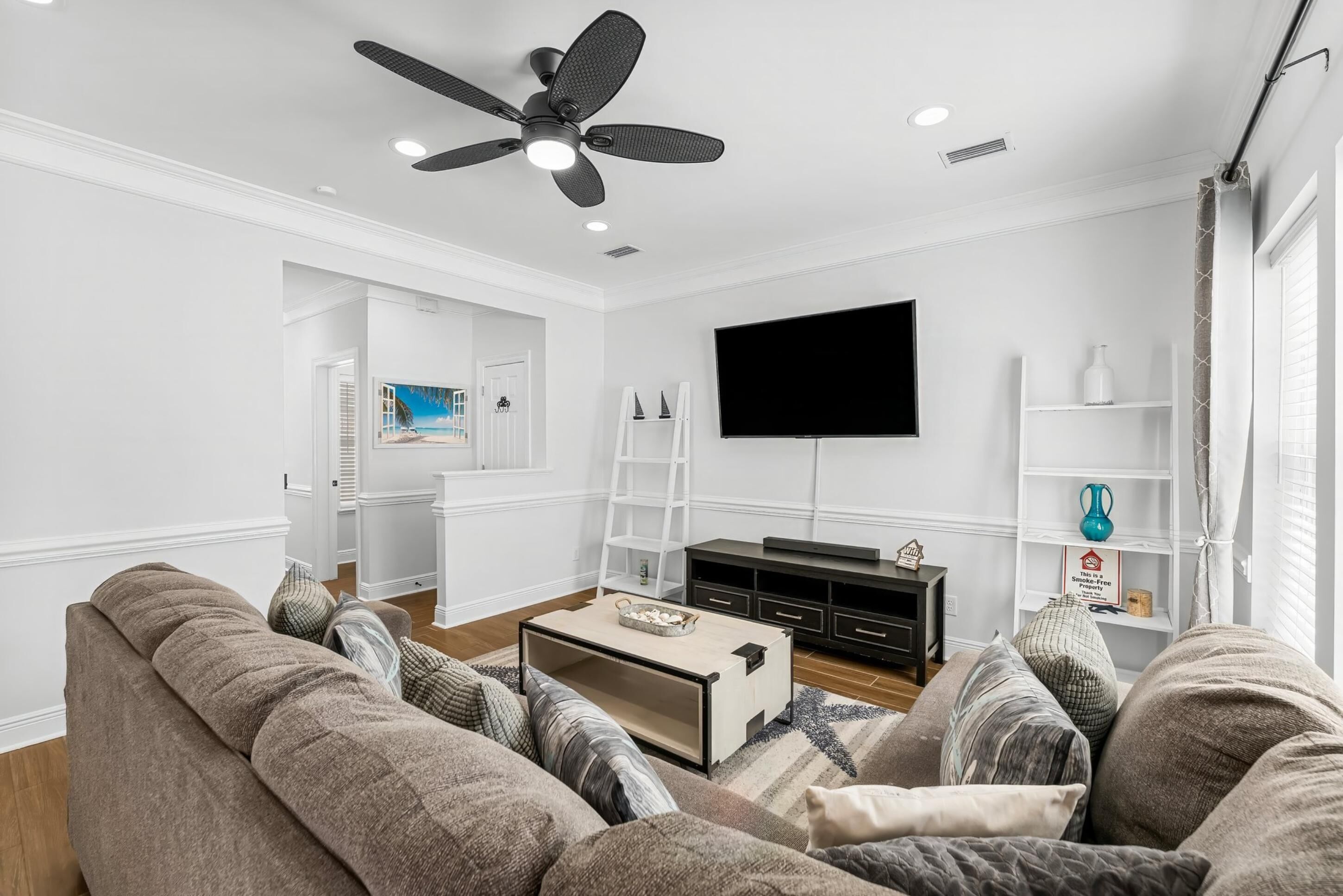 A modern living room with a ceiling fan, a flat-screen TV, and a sofa set.