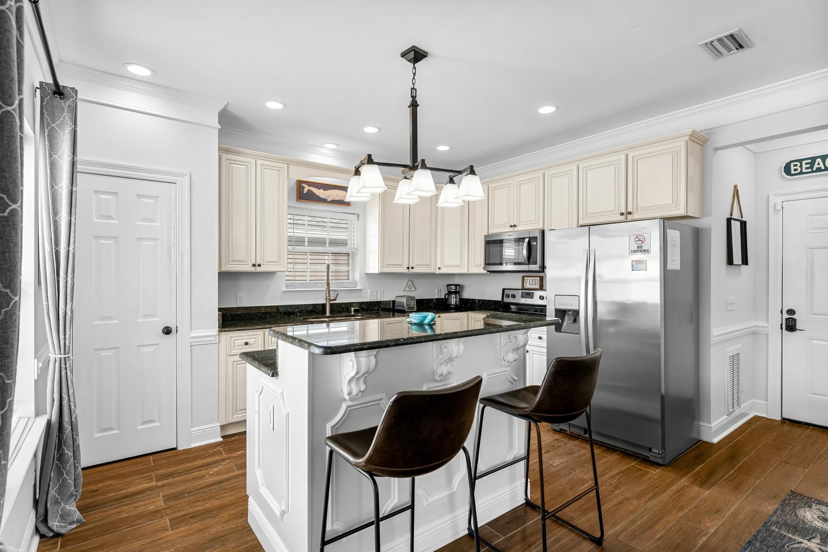 A modern kitchen with white cabinetry, a central island with bar stools, stainless steel appliances, and a pendant light.