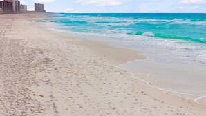A sandy beach with footprints, a calm sea, and buildings in the background. - Pet Friendly Beach House - Sunset Escape (Panama City Beach)