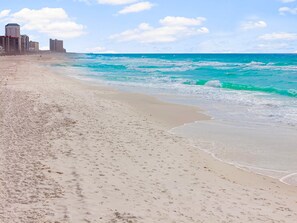 A sandy beach with footprints, a calm sea, and buildings in the background. - Pet Friendly Beach House - Sunset Escape (Panama City Beach)