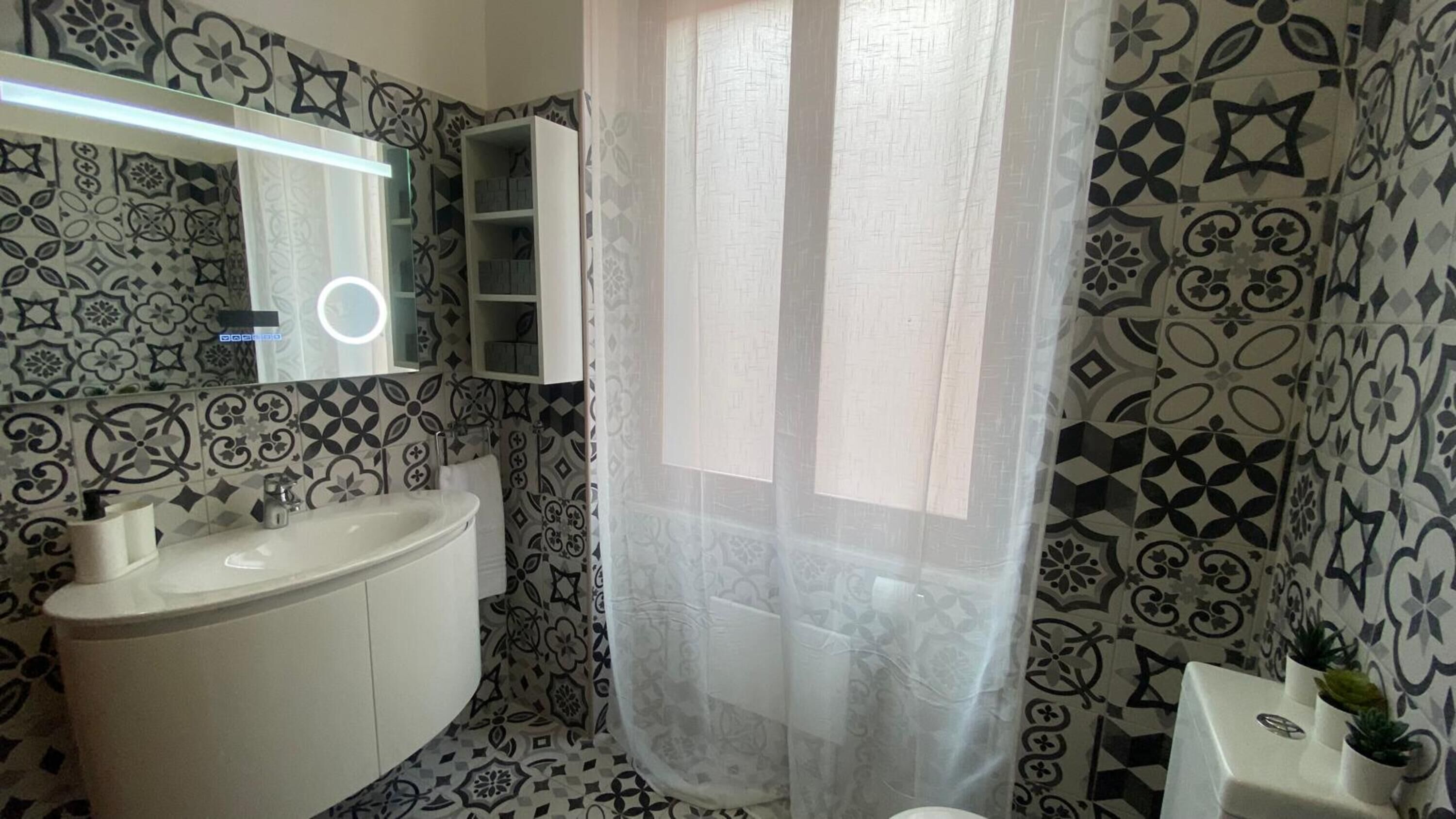Une salle de bain avec des carreaux décorés, un lavabo blanc, un miroir et un rideau de douche.