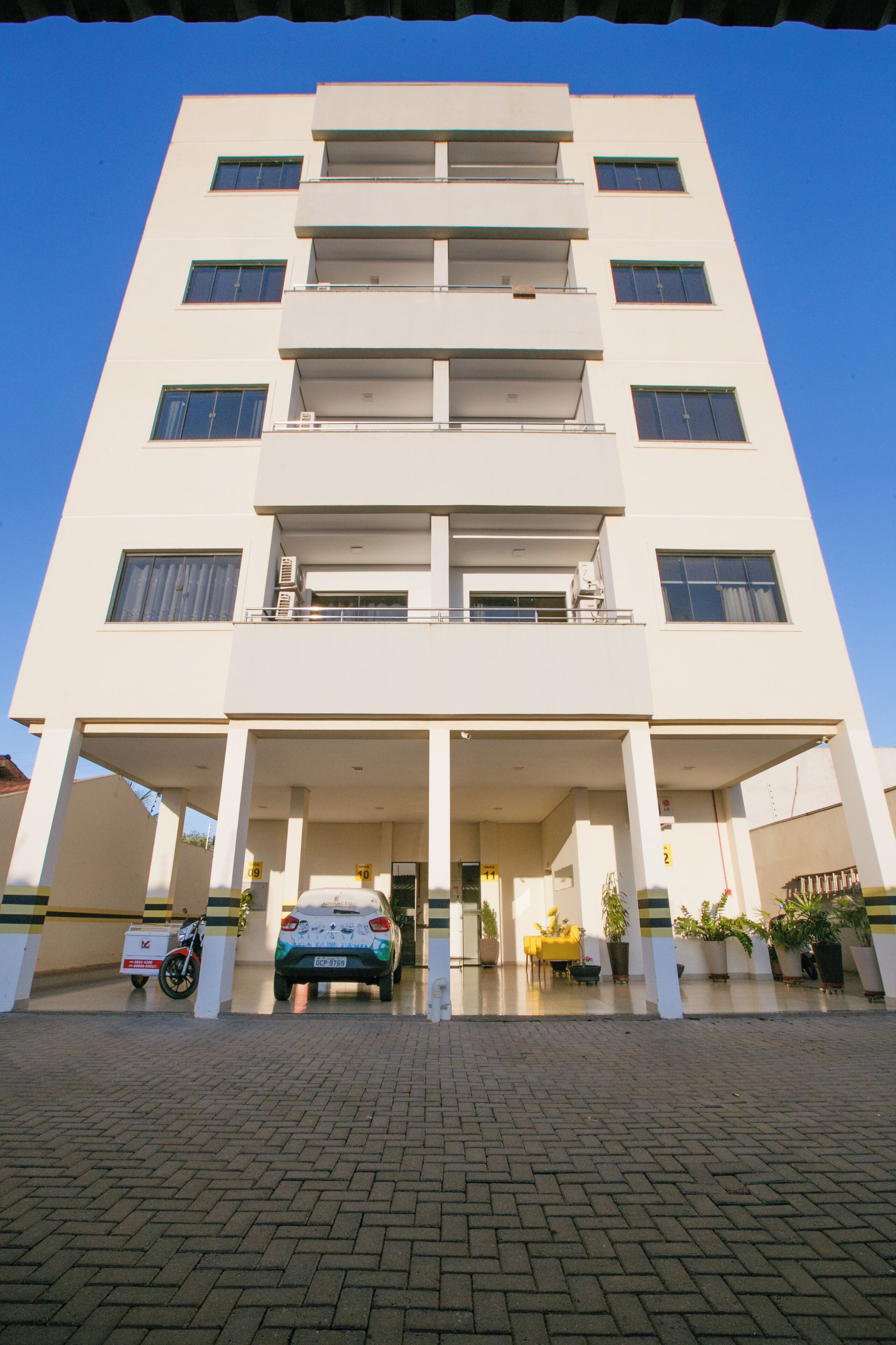 Un edificio de varios pisos con un vestíbulo cubierto, un coche estacionado y una motocicleta.