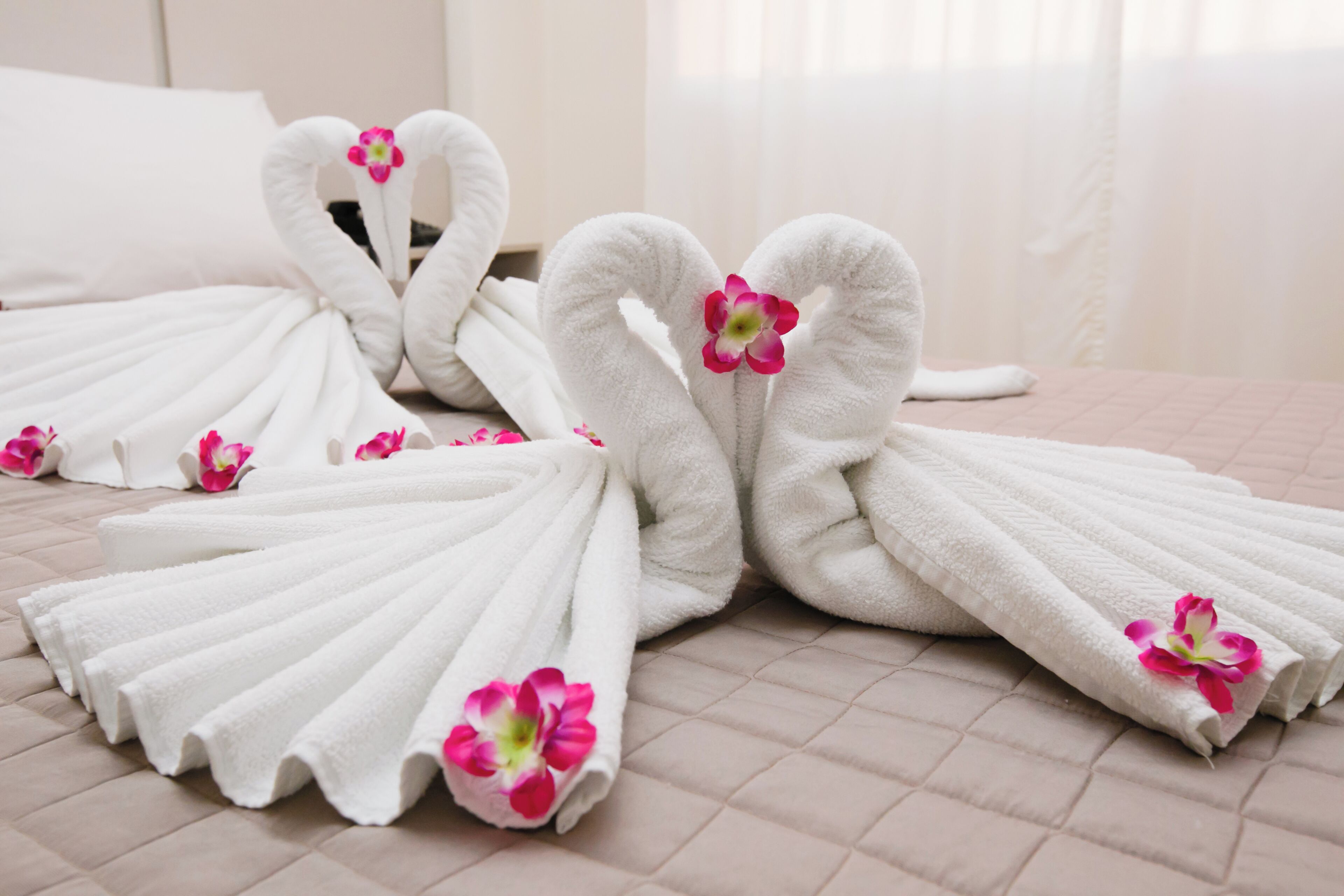 Schoon gerangschikte witte handdoeken gevouwen in de vorm van zwanen, met roze bloemen, op een bed met een roze gebogen deken.
