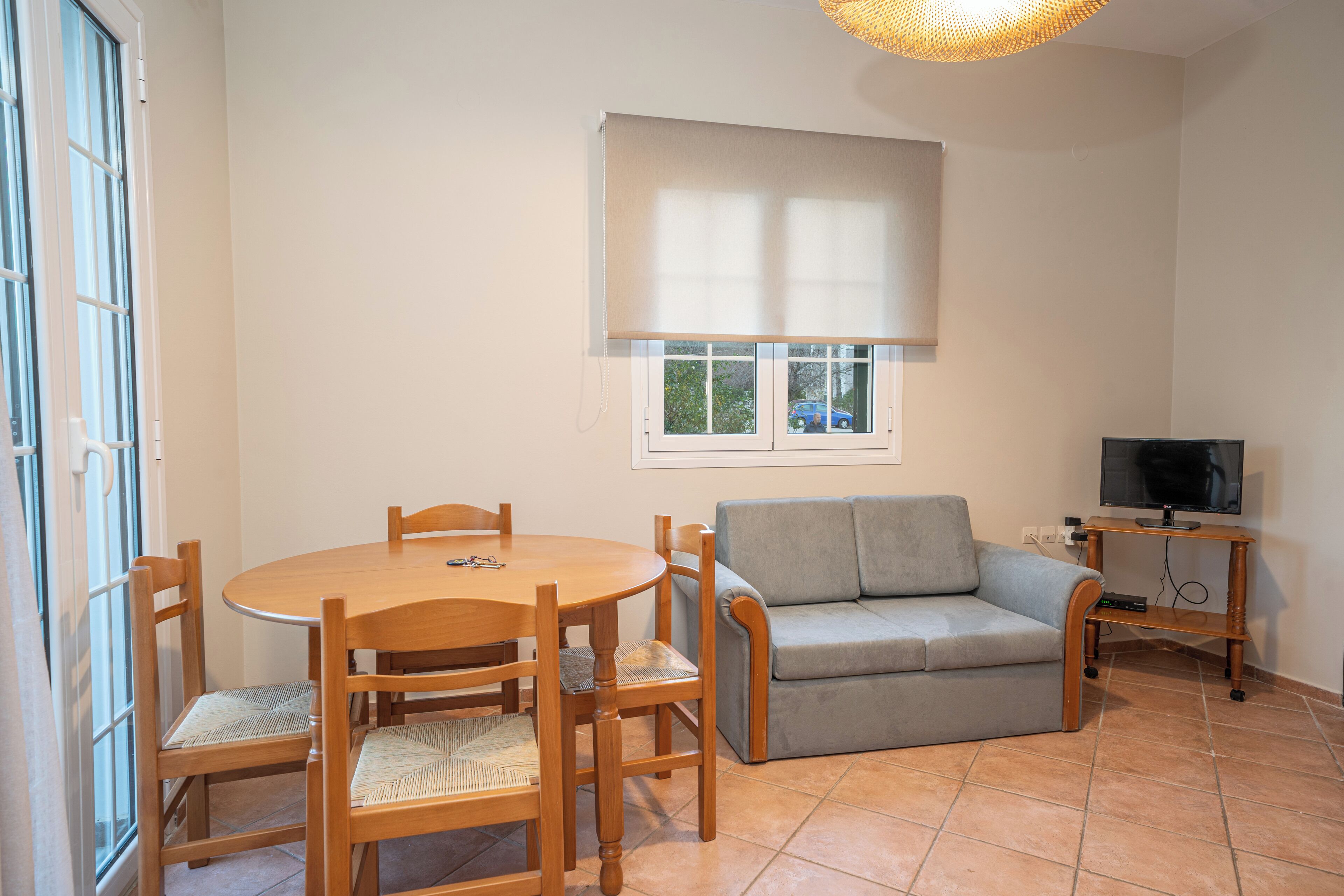 Una sala de estar con una mesa de comedor de madera, un sofá gris y un televisor sobre un mueble de madera.