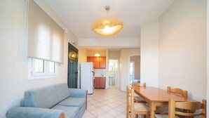 A living room with a sofa, a dining table with chairs, a kitchen in the background, and a ceiling light fixture. - Captain's Villas (Kefalonia)