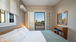 A bedroom with a bed, a dresser, a mirror, and a sliding glass door leading to an outdoor balcony. - Captain's Villas (Kefalonia)