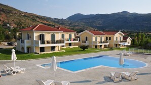 A resort with a swimming pool, lounge chairs, and a mountainous backdrop. - Captain's Villas (Kefalonia)