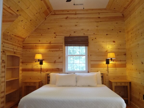 A wooden cabin room with a bed, two wall-mounted lamps, and a window. - New Cabin,Be the First to Book! Private and Peaceful, 140 Acres, River trails! (Faber)
