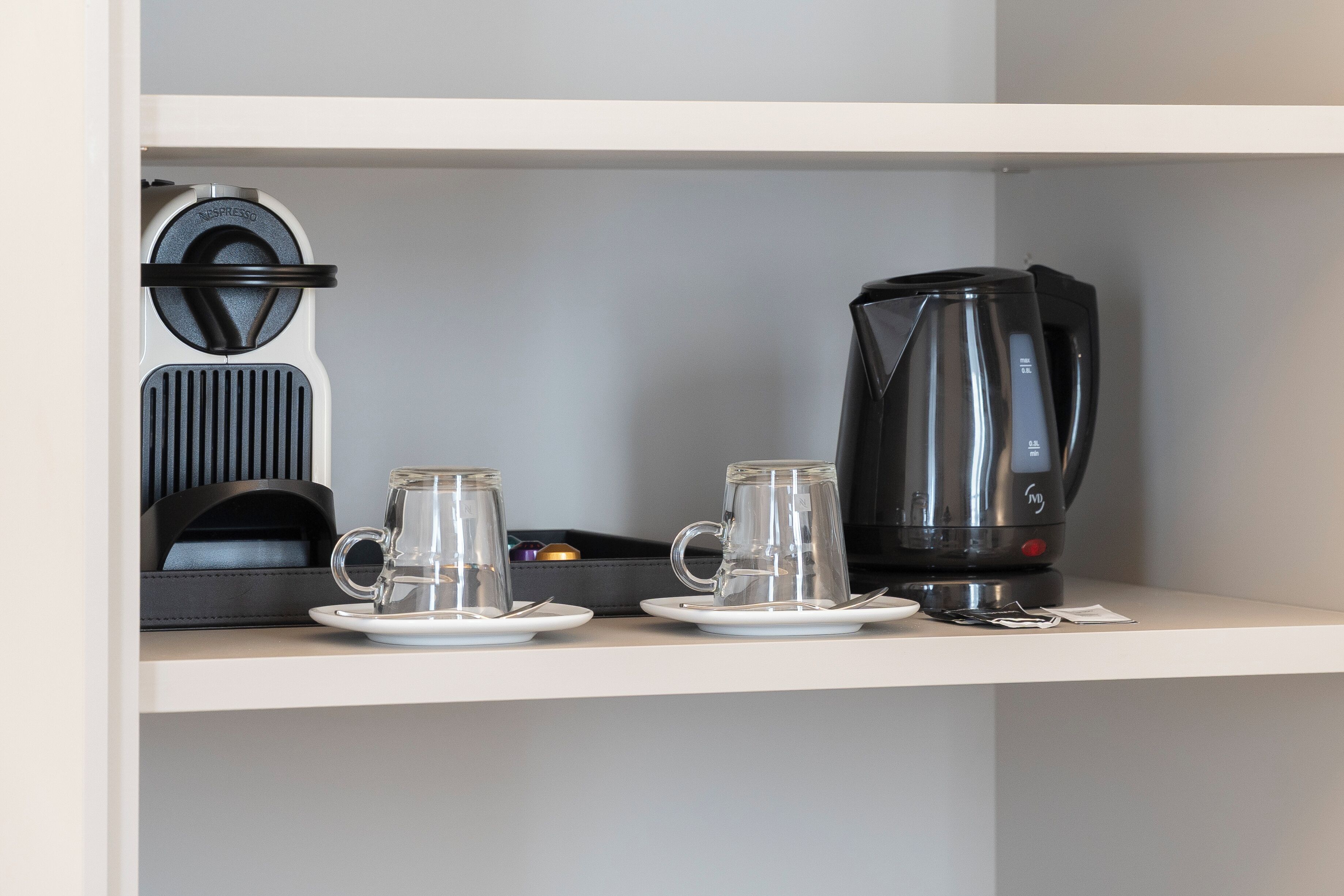 A coffee station with a vintage espresso machine, a modern coffee maker, and two glass cups on a white shelf.