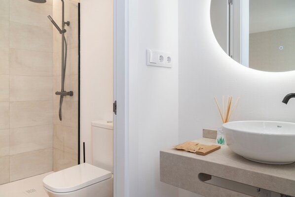 A modern bathroom with a white toilet, a shower with a glass door, and a round mirror above a beige countertop with a white sink.