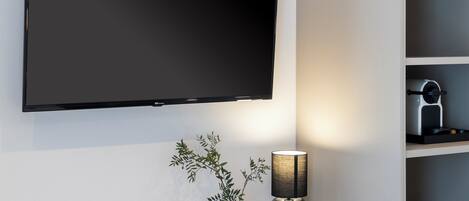 Una sala de estar moderna con un televisor de pantalla plana montado en la pared, una planta decorativa en un jarrón blanco y una lámpara de mesa con pantalla negra.