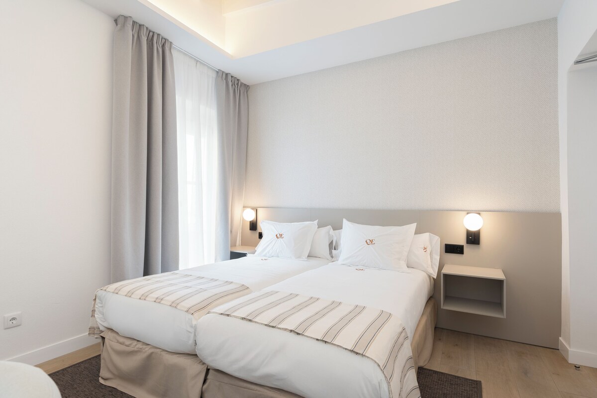 A modern hotel room with a large bed, two bedside tables, and a wall-mounted light fixture.
