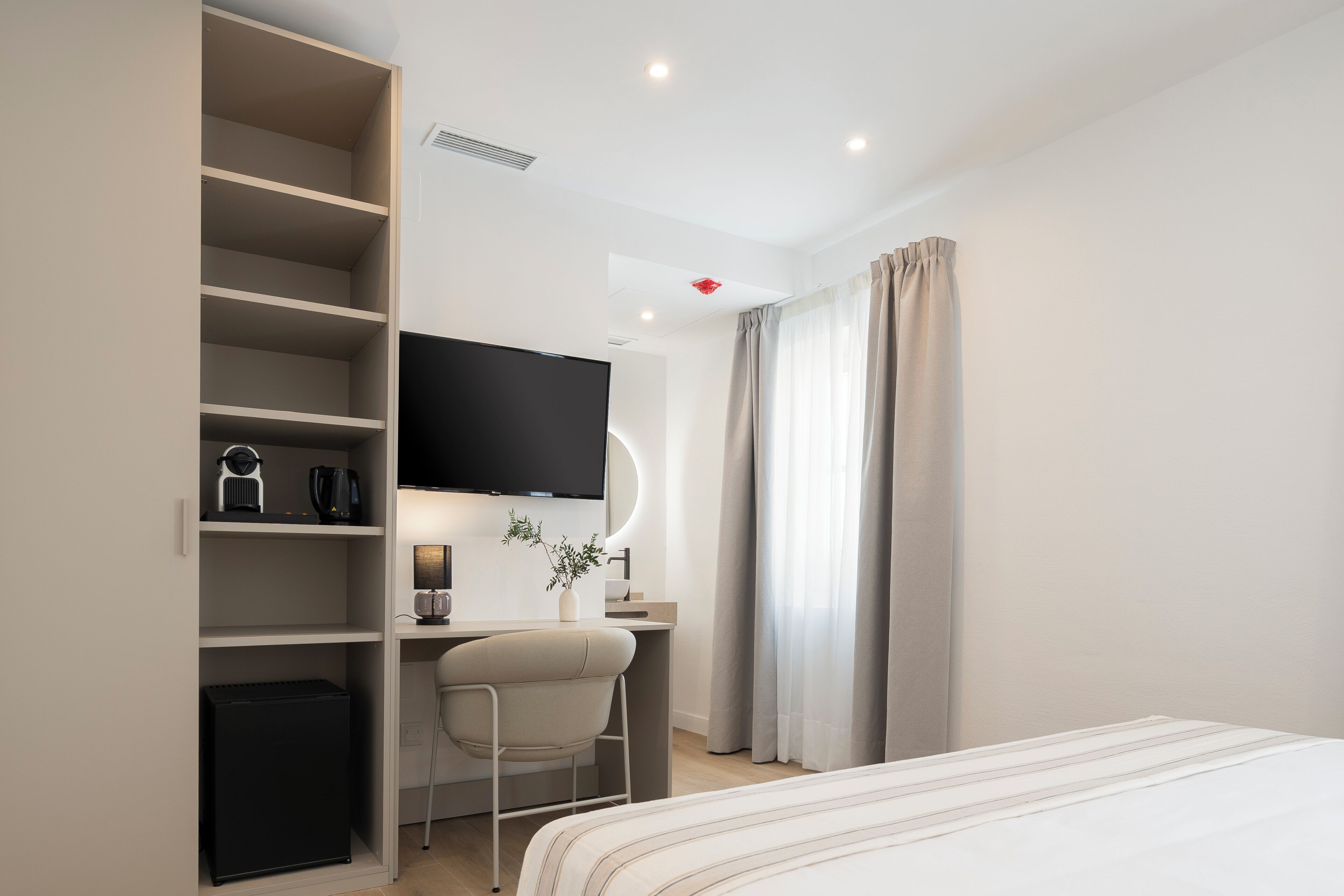 A modern hotel room with a bed, a desk with a chair, a television, and a wardrobe.