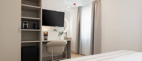 A modern hotel room with a bed, a desk with a chair, a television, and a wardrobe.