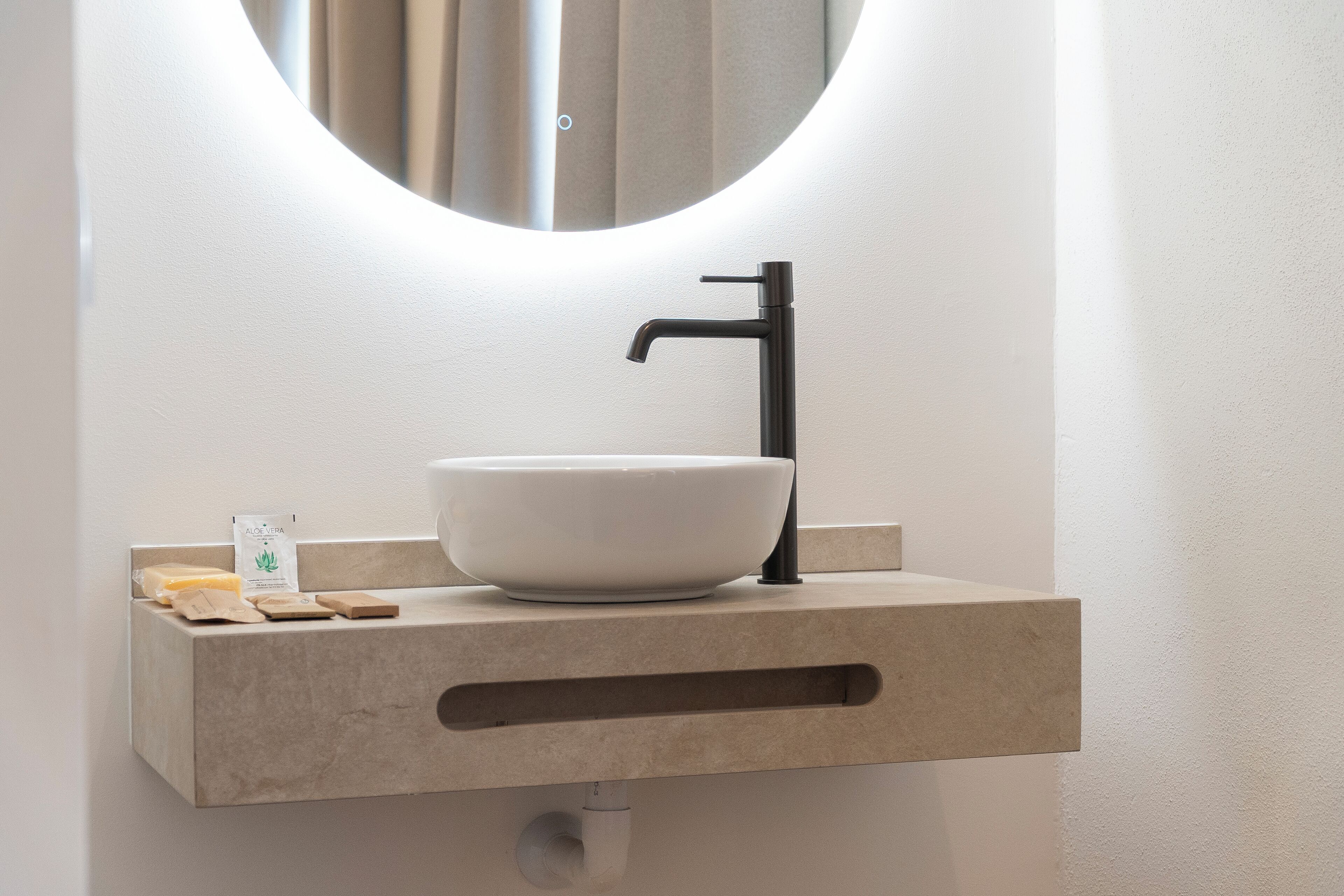 Une salle de bain avec un lavabo blanc, un robinet noir et un miroir au-dessus.