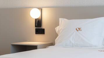 Una habitación de hotel con una cama bien hecha, una mesita de noche, una lámpara de pared y una almohada con un logo.
